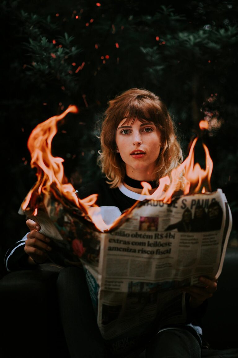 A young woman holding a burning newspaper, creating a dramatic scene.