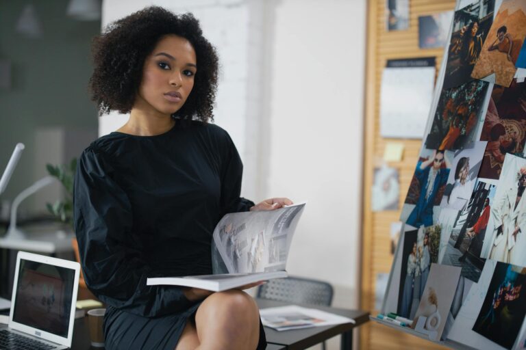 Elegant woman in a black dress holding a magazine in a modern office environment.